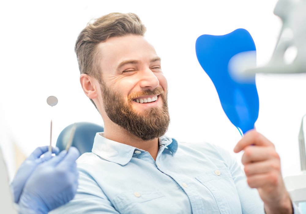 philadelphia invisalign patient model looking into a hand mirror in a dental chair and smiling